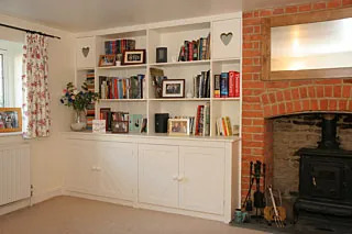 Built-in bookshelves and cupboards in an alcove beside a brick fireplace